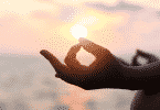Mãos de uma pessoa meditando sob o pôr do sol