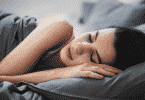 Mulher dormindo serenamente na cama, enrolada em um lençol.