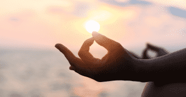 Mãos de uma pessoa meditando sob o pôr do sol