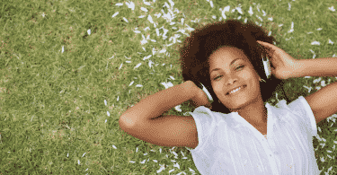 Mulher sorrindo deitada na grama ouvindo música