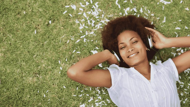 Mulher sorrindo deitada na grama ouvindo música