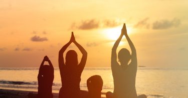 Família praticando Yoga juntos em uma praia.