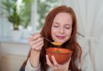 Menina tomando uma sopa com os olhos fechados.