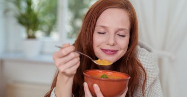 Menina tomando uma sopa com os olhos fechados.