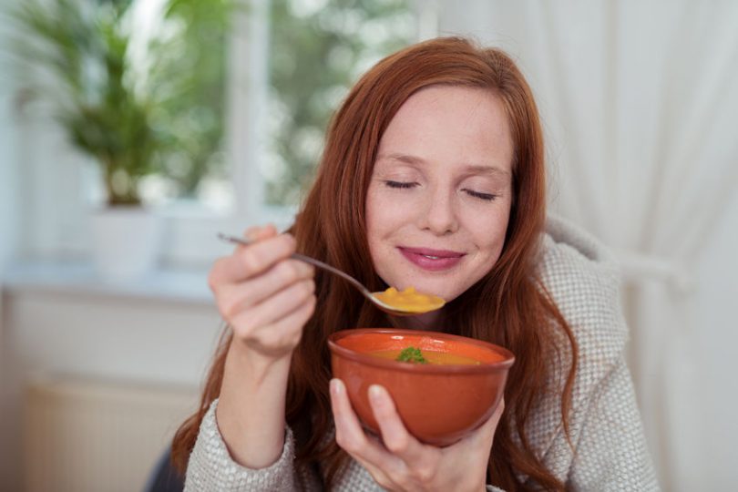 Menina tomando uma sopa com os olhos fechados.