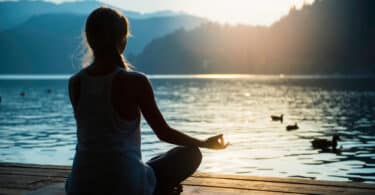 Pessoa sentada meditando em frente a um lago