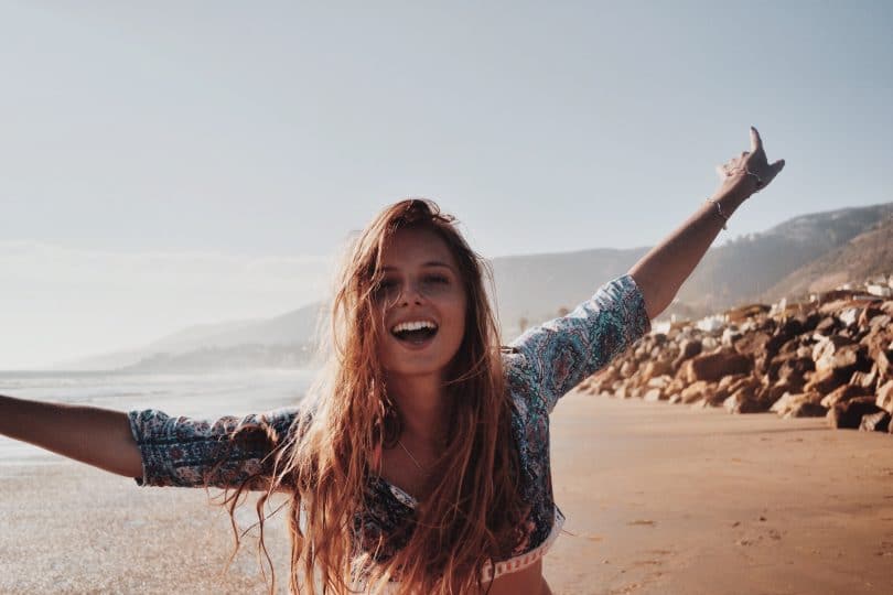 Mulher na praia com os braços abertos