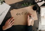 Pessoa escrevendo em uma folha ao lado de um potinho de tinta