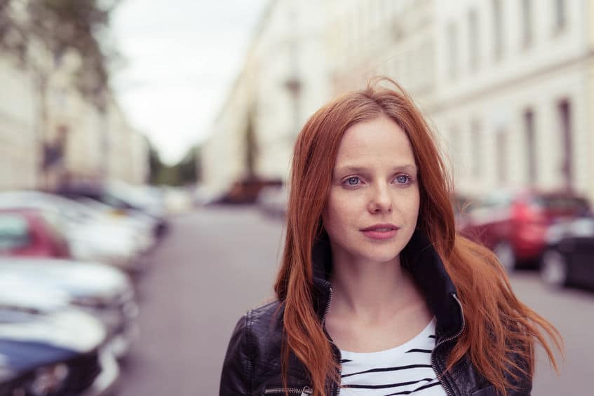 Mulher ruiva parada em meio à rua, olhando ao longe.