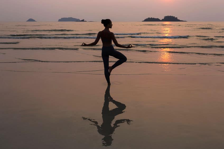 Silhueta de uma mulher fazendo uma pose de yoga à beira do mar.