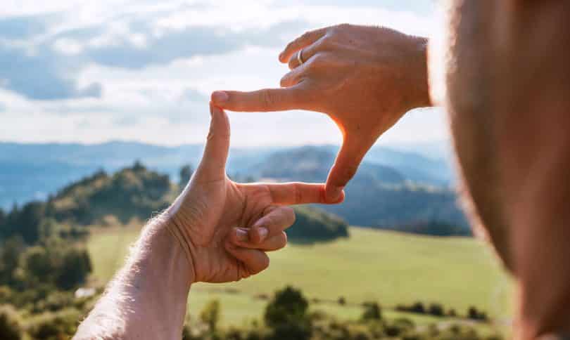 Homem olha para o horizonte, enquadrando-o com os dedos.