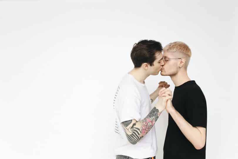 Casal de homens de mãos dadas se beijando