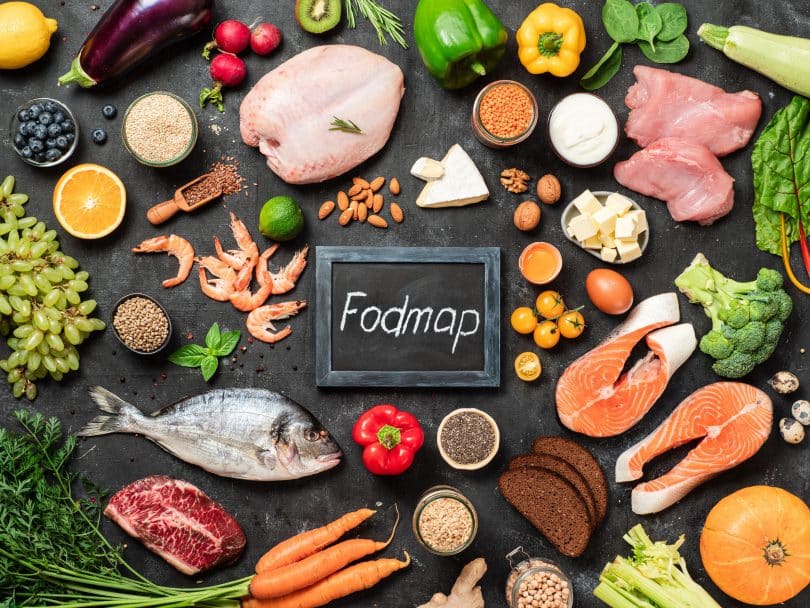 Carne de frango, peixe, frutos do mar, vegetais e frutas e palavras Fodmap no centro, em fundo escuro.