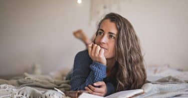 Mulher branca deitada numa cama lendo um livro.