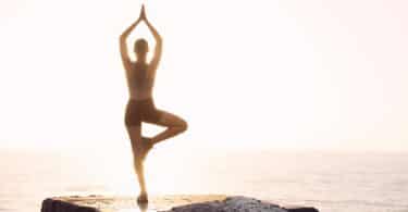 Imagem de uma mulher fazendo Yoga em cima de uma pedra de frente para o mar