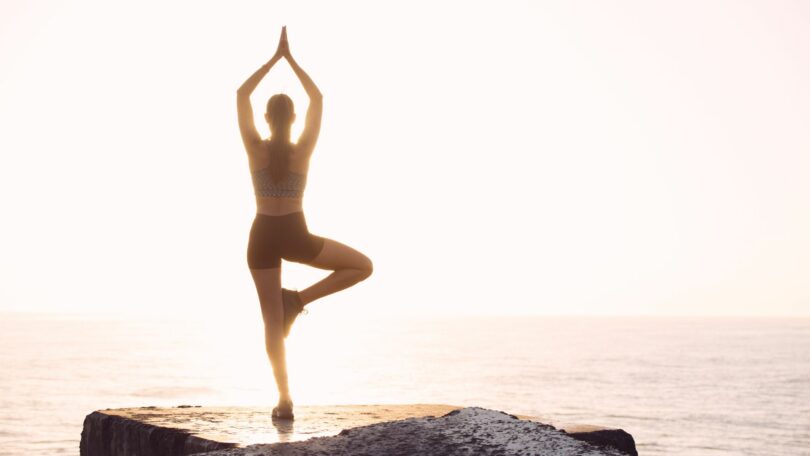 Imagem de uma mulher fazendo Yoga em cima de uma pedra de frente para o mar