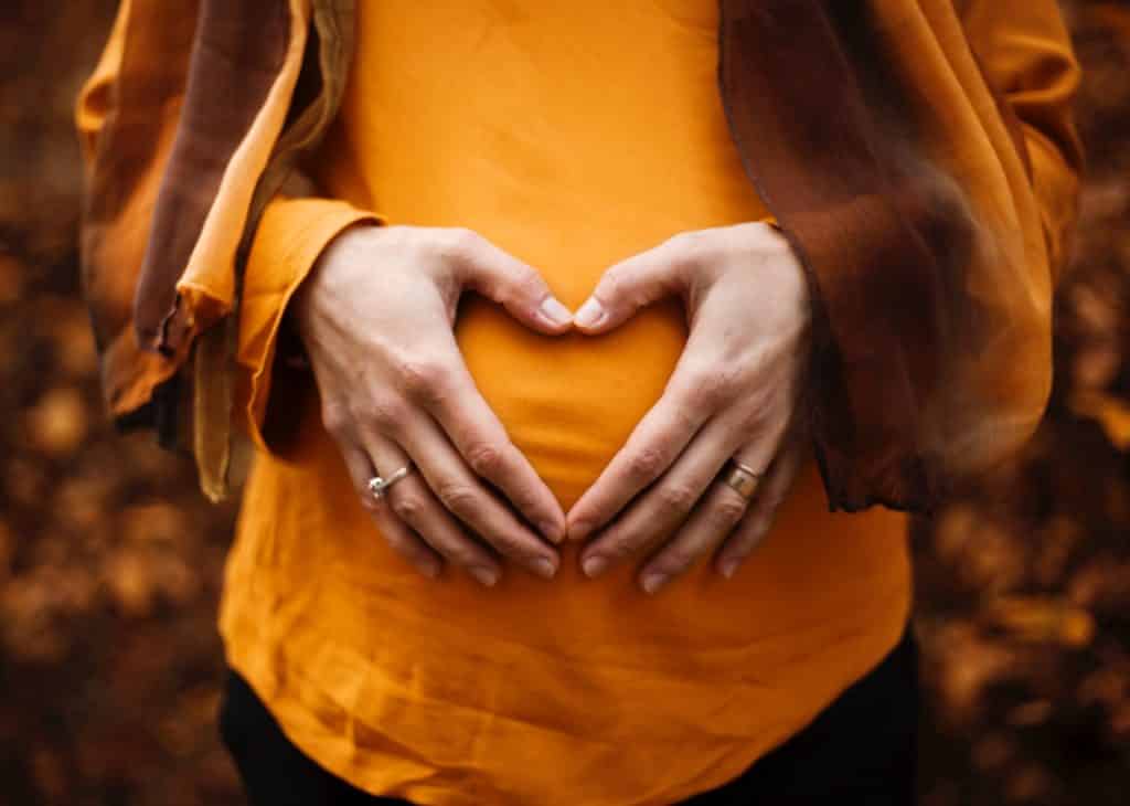 Mulher grávida vista de frente com as mãos sobre sua barriga.