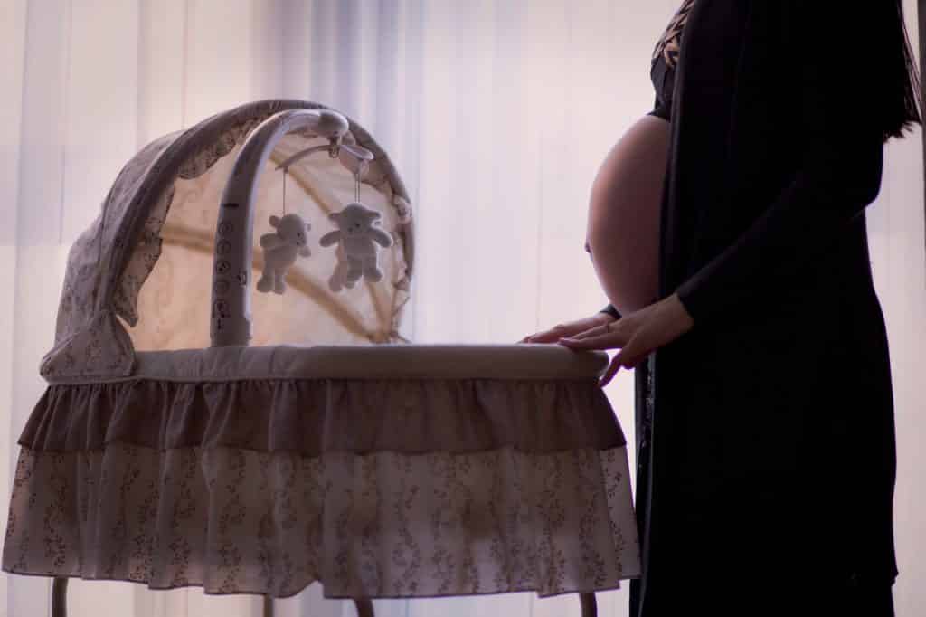 Mulher grávida vista de perfil, tocando o carrinho de seu futuro bebê.