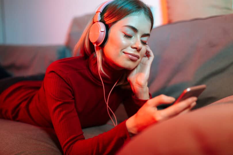 Mulher com os olhos fechados, deitada no sofá ouvindo música enquanto segura o celular.