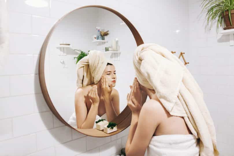 Mulher se olhando no espelho com toalha na cabeça