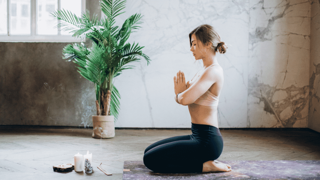 Mulher meditando e uma sala aberta com uma planta e algumas velas acesas