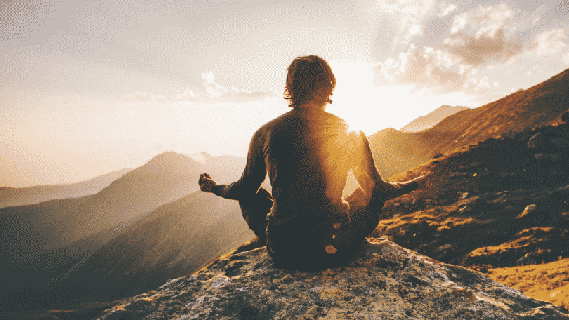 Homem meditando nas montanhas sob o pôr do sol