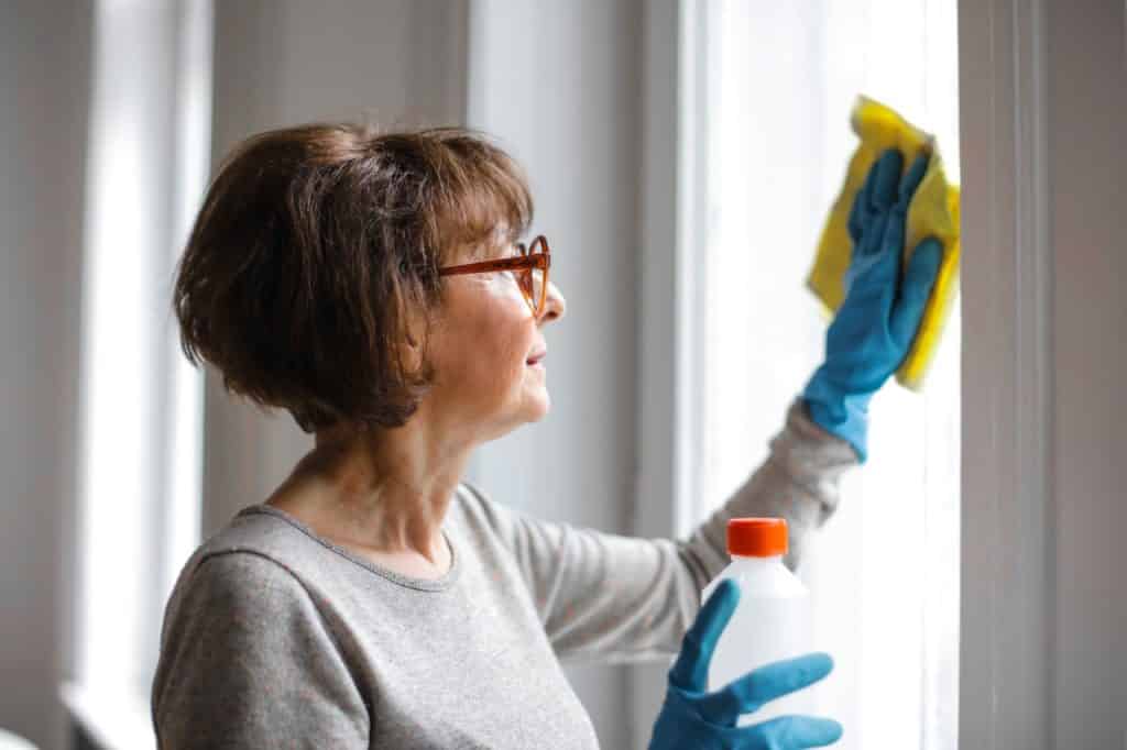 Mulher limpando as janelas de sua casa com luvas de borracha.