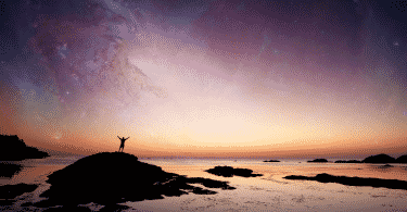 Pessoa com os braços erguidos na praia contemplando o universo