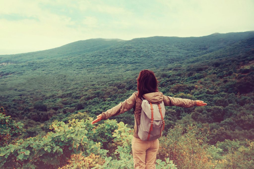 Mulher de costas com braços aberto em montanha com paisagem de natureza