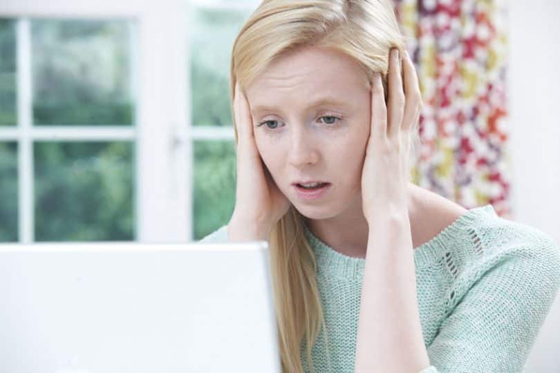 Garota assustada vendo notebook com mãos na cabeça