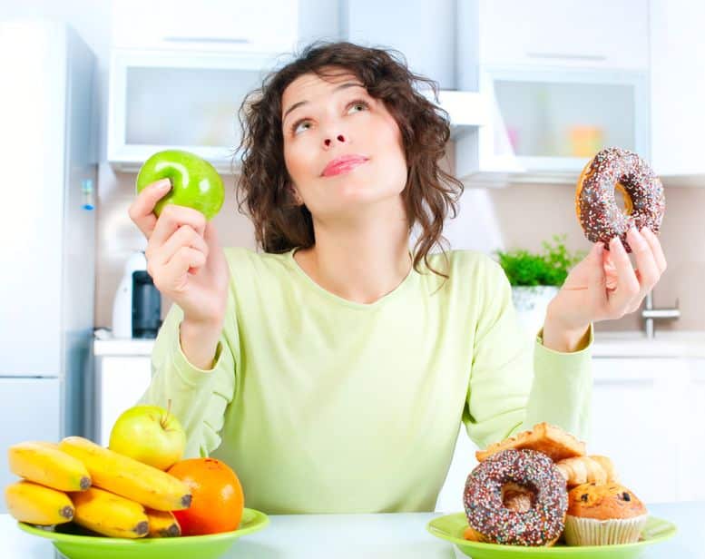 Mulher com olhar pensativo segurando um donut e uma maçã.