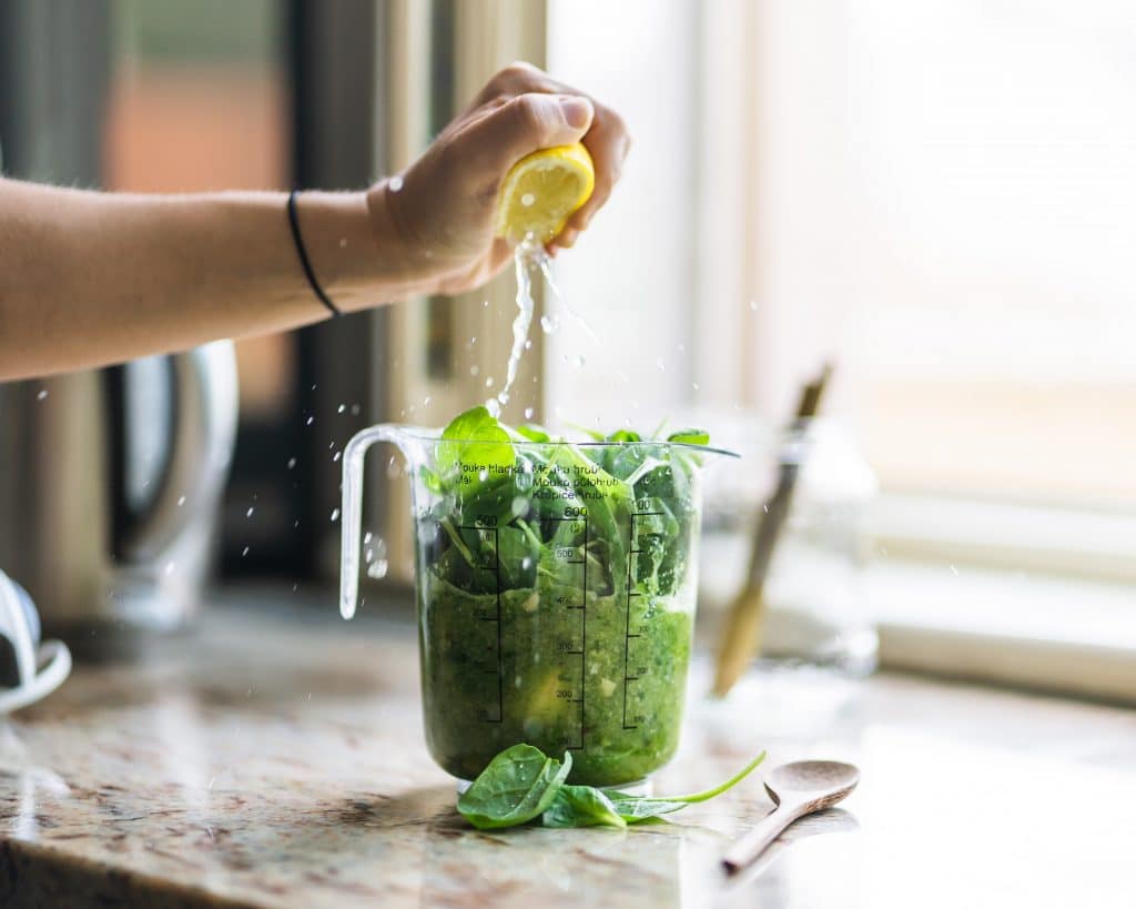 Pessoa espremendo um limão em uma vitamina verde, com folhas de espinafre.