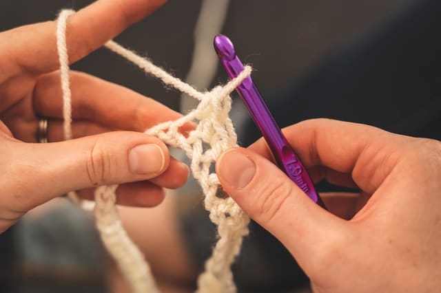 Foco em mãos tricotando com uma agulha de crochê.