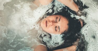 Mulher em uma banheira com espuma, com os braços e o rosto para fora da água.