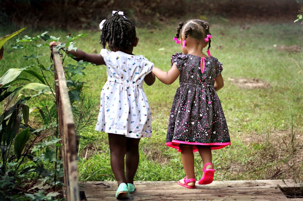 Duas meninas crianças caminhando de mãos dadas por um parque.