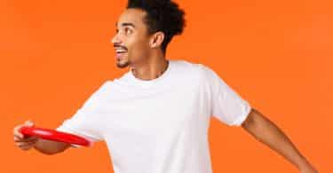 Homem negro usando camiseta branca, jogando disco vermelho.