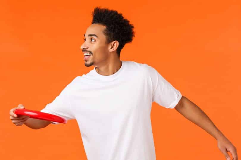 Homem negro usando camiseta branca, jogando disco vermelho.