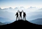 Três pessoas no topo da montanha com os braços levantados