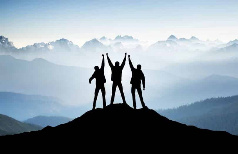 Três pessoas no topo da montanha com os braços levantados