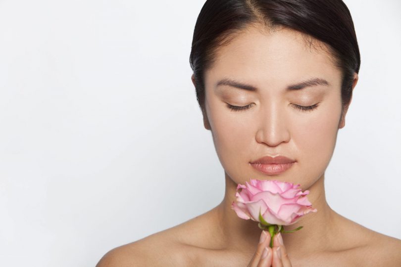 Mulher asiática com os olhos fechados segurando flor rosa.