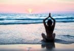 Mulher de costas meditando na praia.