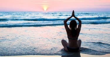 Mulher de costas meditando na praia.