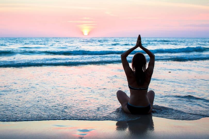 Mulher de costas meditando na praia.