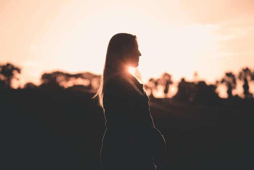 Mulher de olhos fechados sendo iluminada pelo pôr do sol