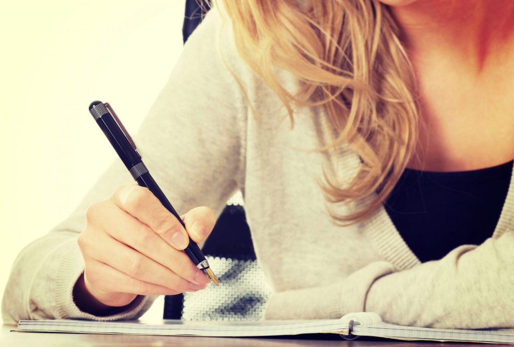 Mulher segurando caneta, prestes a escrever em um caderno.