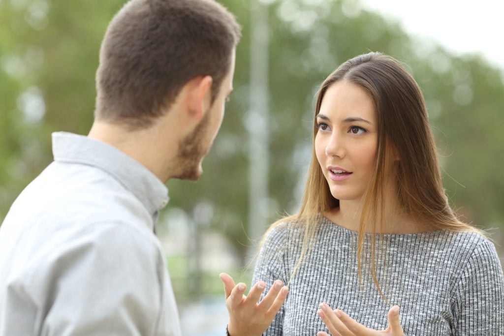 Mulher discutindo com um homem, e gesticulando com as mãos.