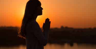 Silhueta de uma mulher com as mãos em pose de oração.