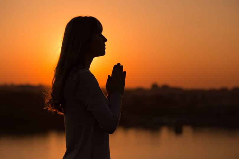 Silhueta de uma mulher com as mãos em pose de oração.