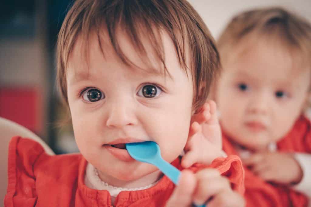 Bebê com colher na boca olhando para frente.