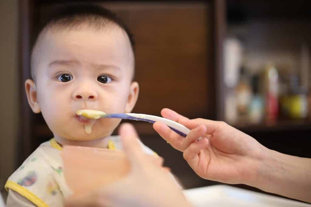 Bebê olhando enquanto mulher leva em sua boca uma colher com papinha.